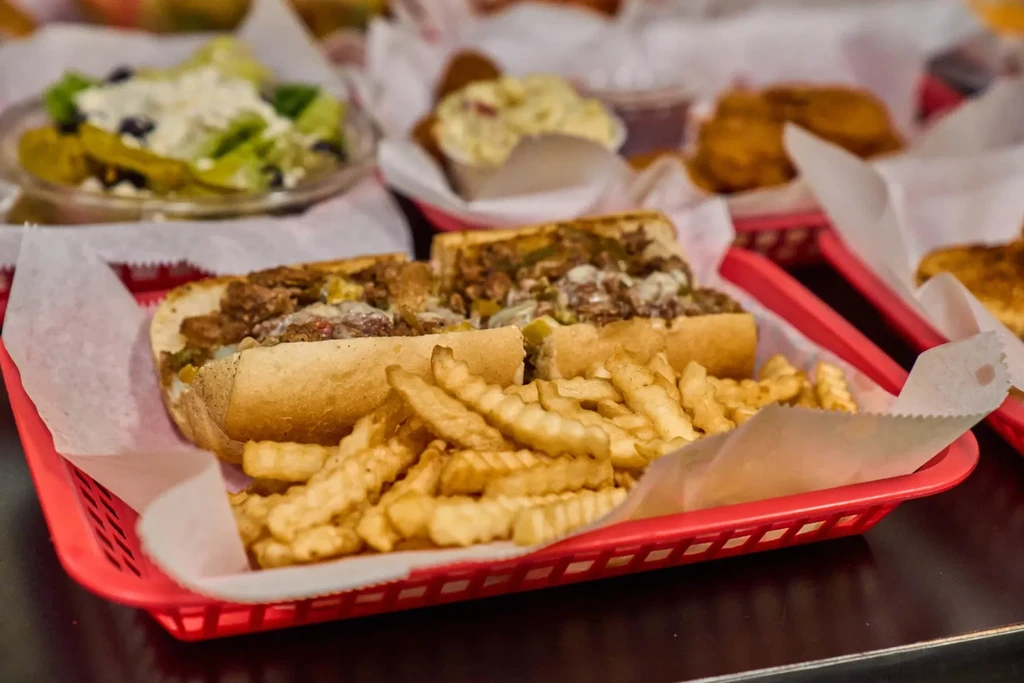 Steak and cheese sub sandwich with crinkle-cut fries in a red basket.