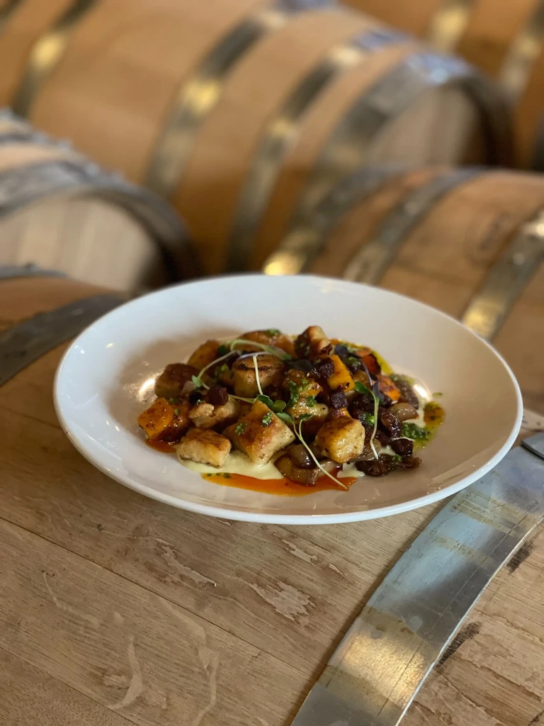 Plated gnocchi dish with vegetables, berries, sauces on a wine barrel.
