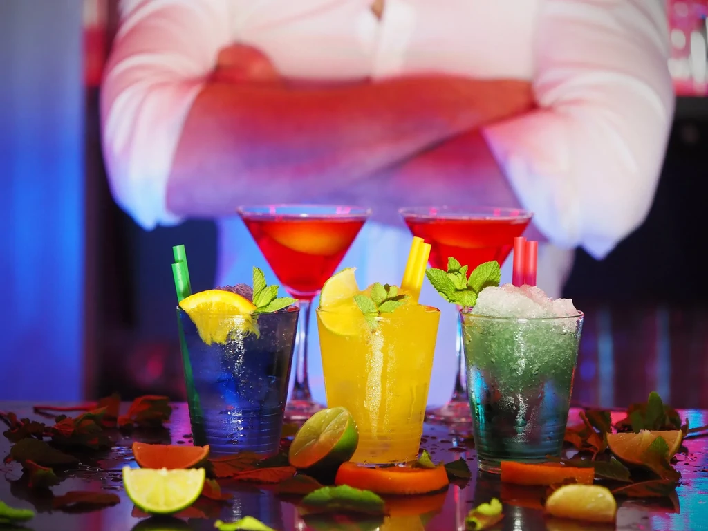 Colorful cocktails with citrus and mint on a dark bar, person visible.
