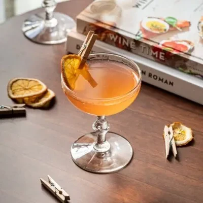 Amber cocktail in vintage coupette with dried orange, clothespin on wood.