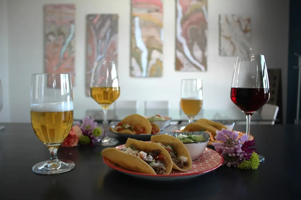 Hard-shell tacos, guacamole, beer, and wine on a decorated dining table.