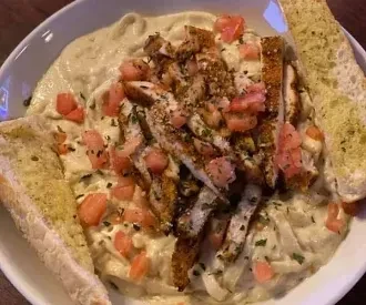Creamy pasta with grilled chicken, tomatoes, herbs, and garlic bread.