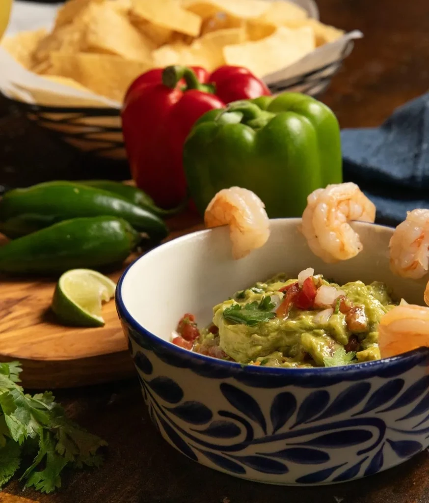 Guacamole bowl with shrimp, garnished with tomatoes, onions, cilantro.
