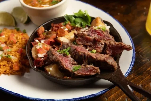 Cast iron skillet with steak, potatoes, pico de gallo, and rice.