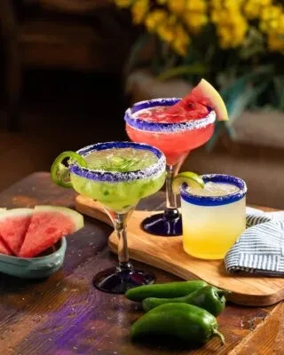 Three margaritas with jalapeños and watermelon on a rustic wooden surface.