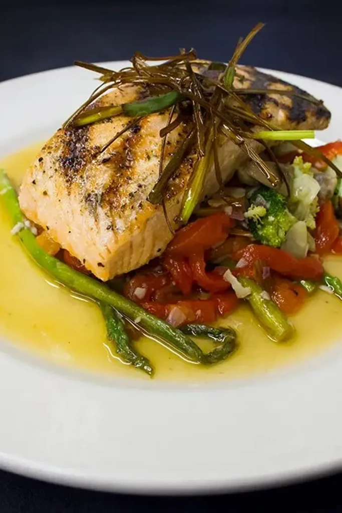Grilled salmon fillet, vegetables, and golden sauce on a white plate.
