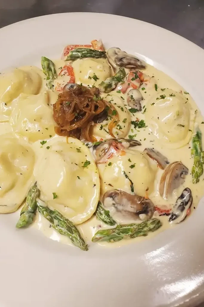 Ravioli in creamy sauce with asparagus, clams, crispy shallots, and herbs.