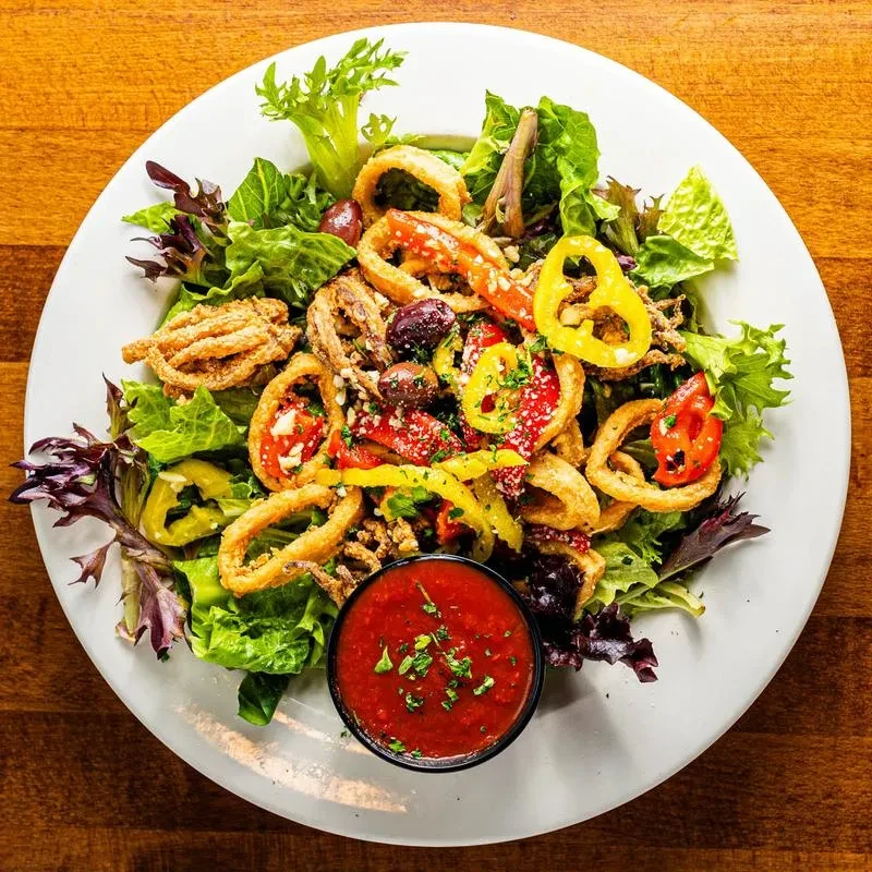 Fried calamari salad with mixed greens, vegetables, cheese, and sauce.