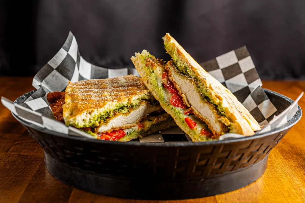 Panini cut in half, showing chicken, pesto, cheese, and red peppers.