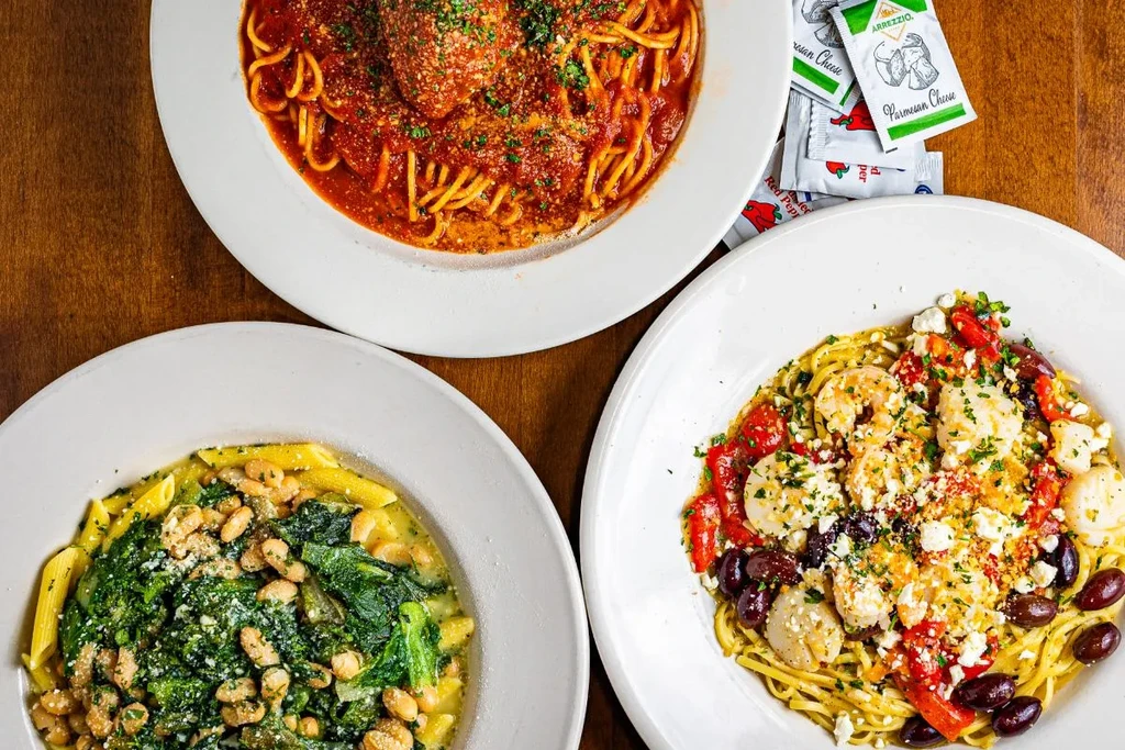 Overhead view of three different pasta dishes on a wooden table.