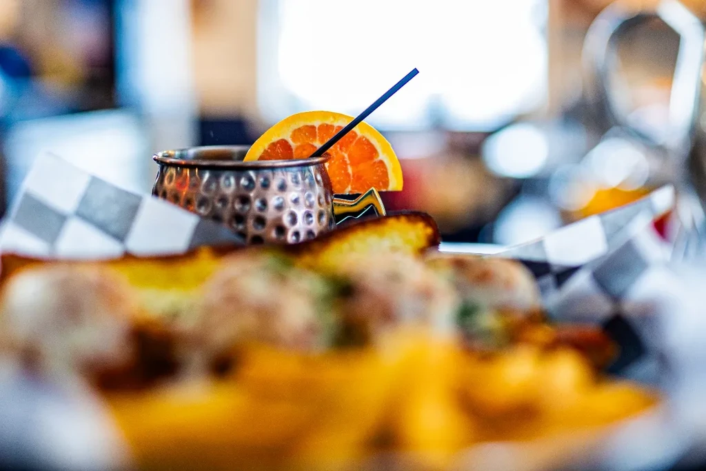Copper mug drink with orange slice, blue straw, and blurred food.