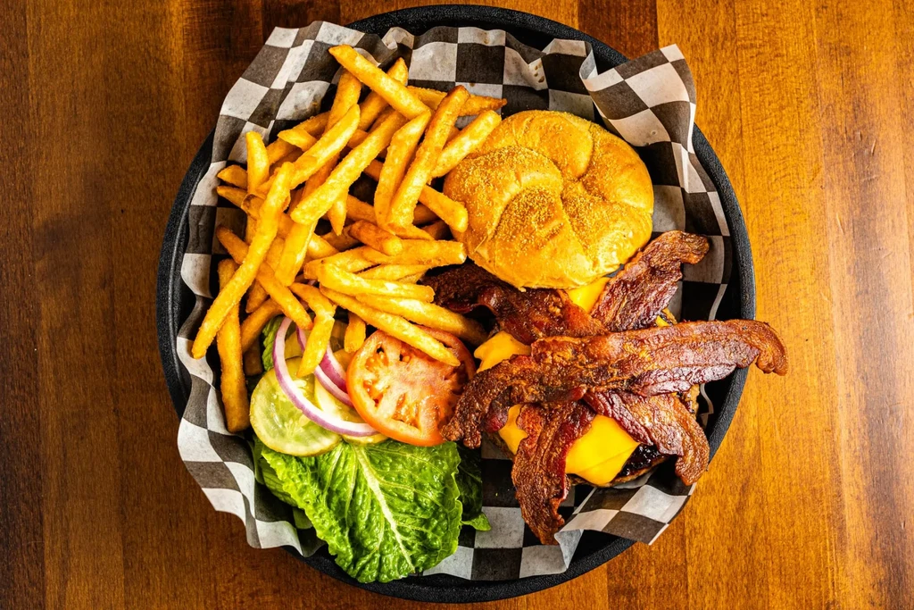 Deconstructed bacon cheeseburger, fries, and fresh toppings in a basket.