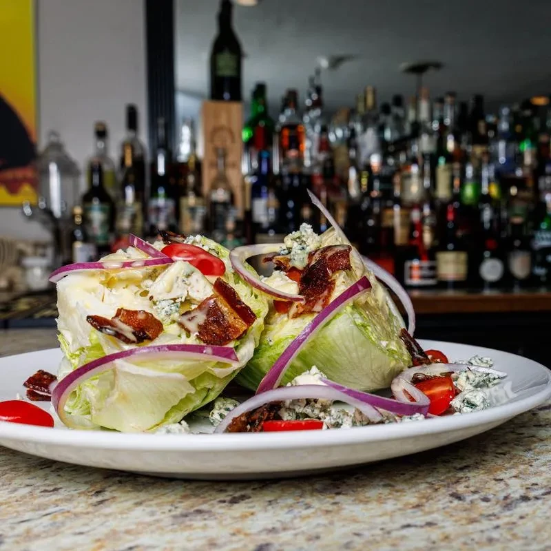 Plated wedge salad with blue cheese, bacon, and tomatoes, bar background.
