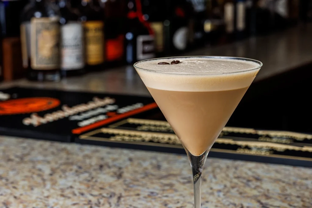 Close-up of an espresso martini with coffee beans on a bar.