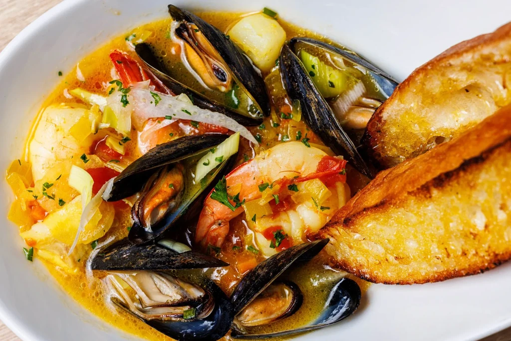 Vibrant seafood stew with mussels, shrimp, vegetables, and toasted bread.