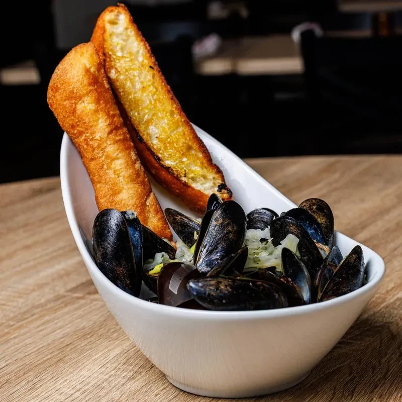 Close-up of steamed mussels in broth with two slices of toasted bread.