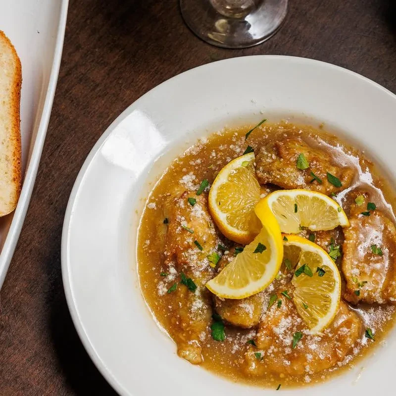 Saucy chicken or veal piccata with lemon slices in a bowl.