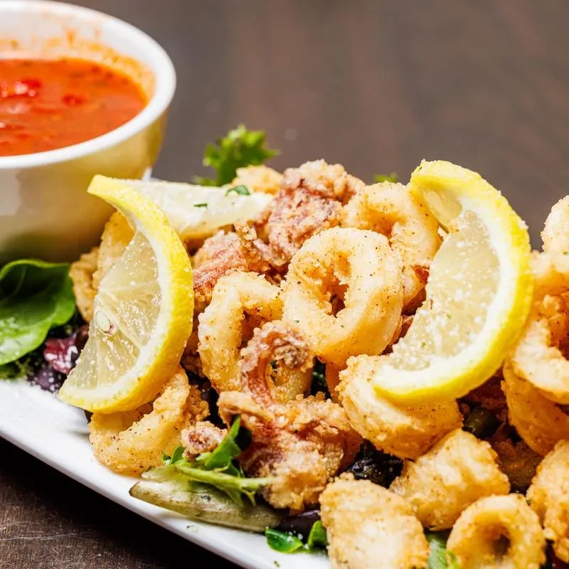 Plate of crispy fried calamari with lemon and red dipping sauce.