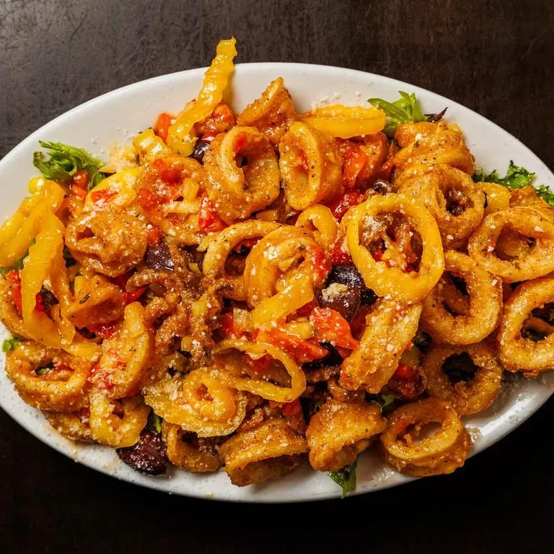 Crispy fried rings with red peppers, olives, and green leaves on plate.
