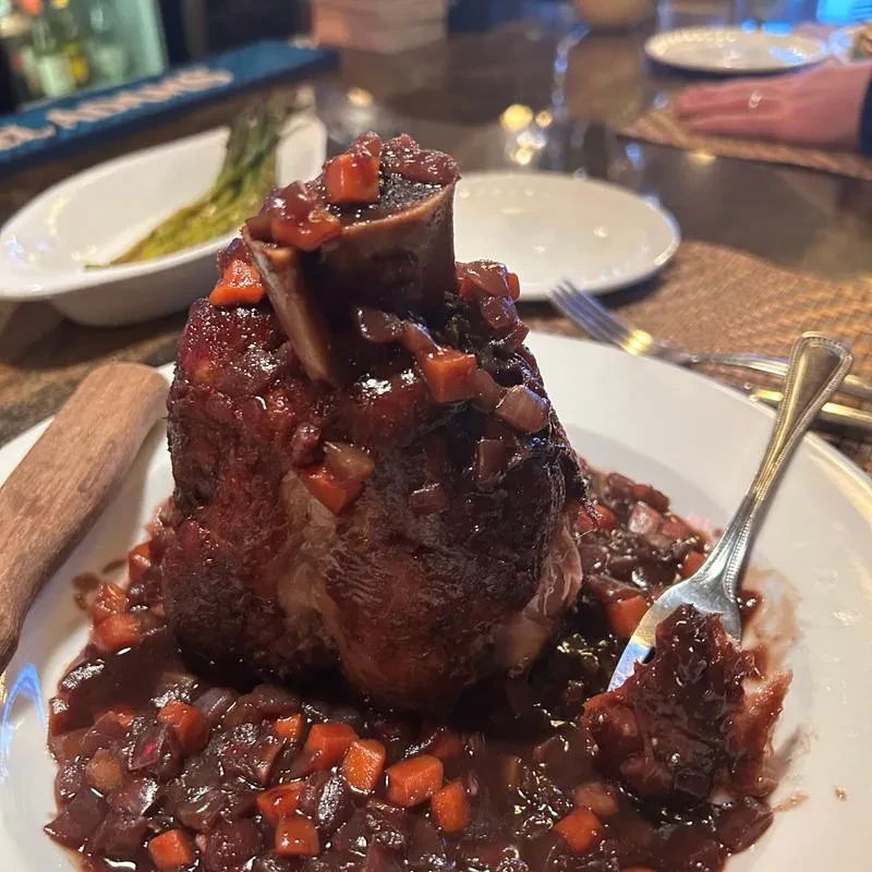 Braised meat shank with sauce and vegetables, fork digging in.