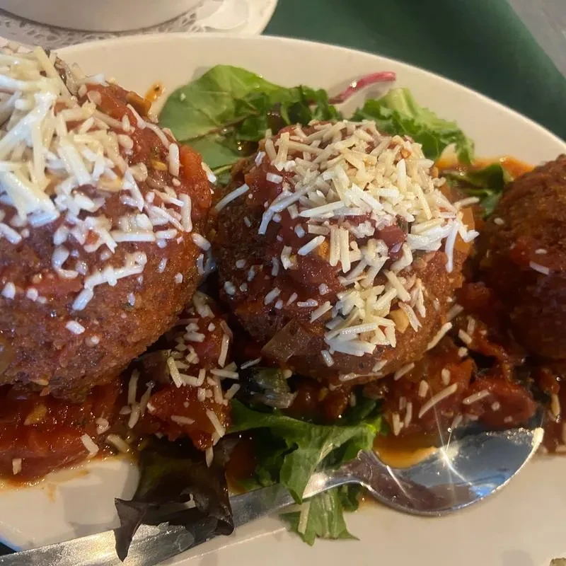 Three breaded arancini or meatballs with tomato sauce, cheese, and greens.