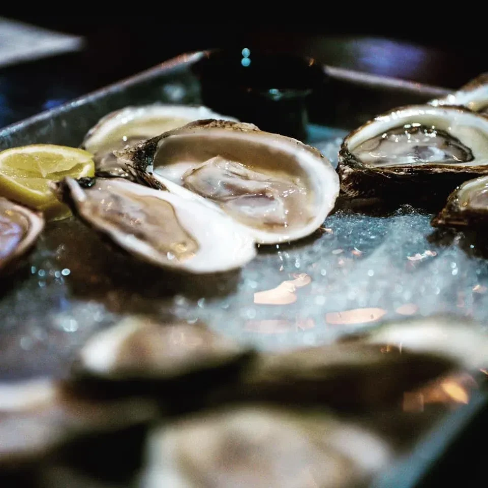 Platter of fresh oysters on crushed ice, with a lemon wedge.