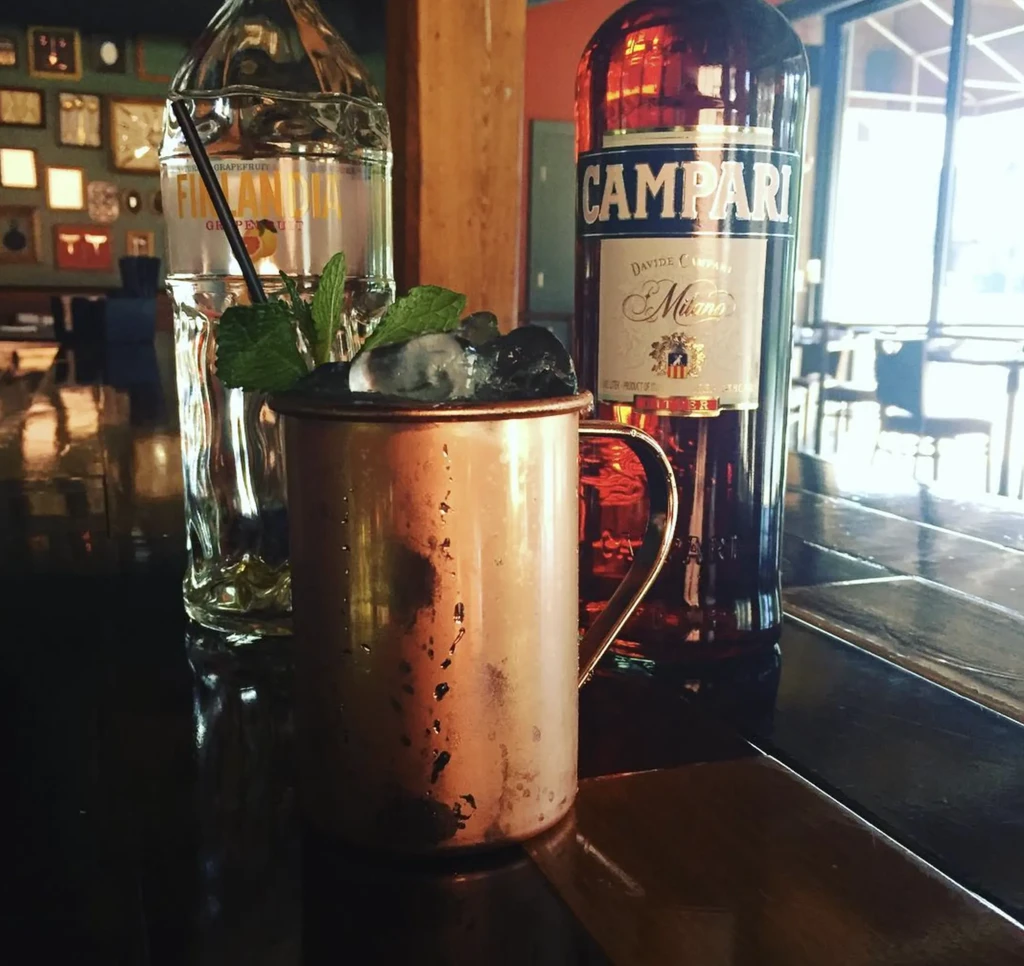 Mint cocktail in copper mug, Campari and vodka bottles on a bar.