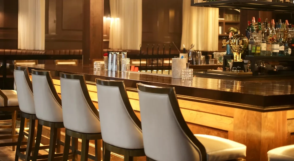 Upscale wooden bar, white stools, neatly arranged drinks, warm lighting.