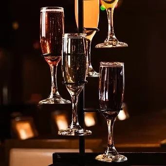 Five champagne flutes with various colored sparkling drinks on a dark stand.