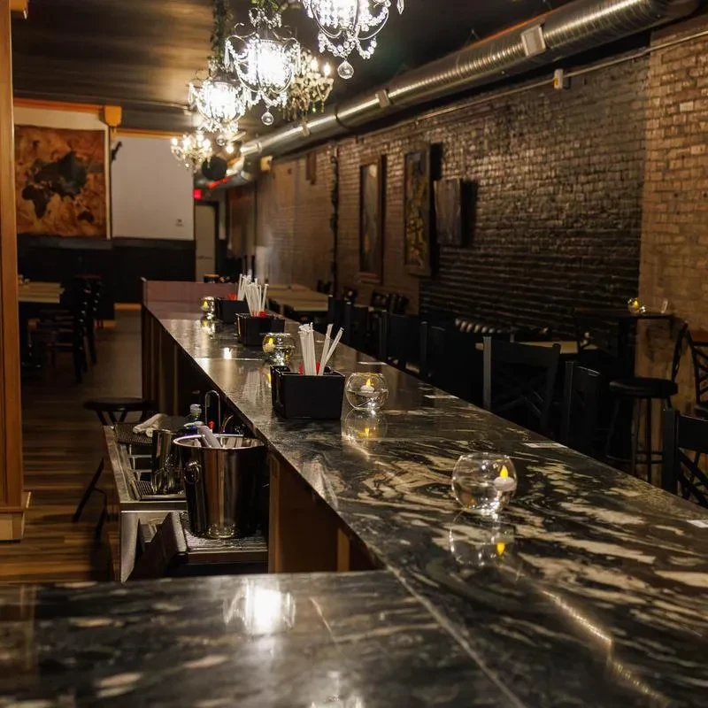 Dark marble bar, crystal chandeliers, and exposed brick in dim interior.