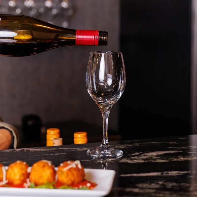 Dark wine bottle pouring into glass, next to arancini with red sauce.