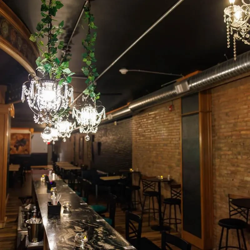 Unoccupied bar with dark marble counter, crystal chandeliers, exposed brick.