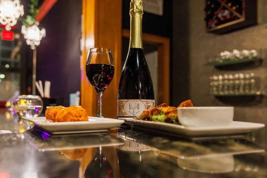Legacy Brut sparkling wine, red wine, and appetizers on a reflective counter.