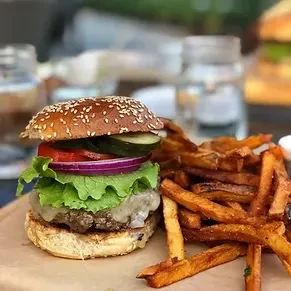 Gourmet beef burger with cheese, vegetables, and golden sweet potato fries.