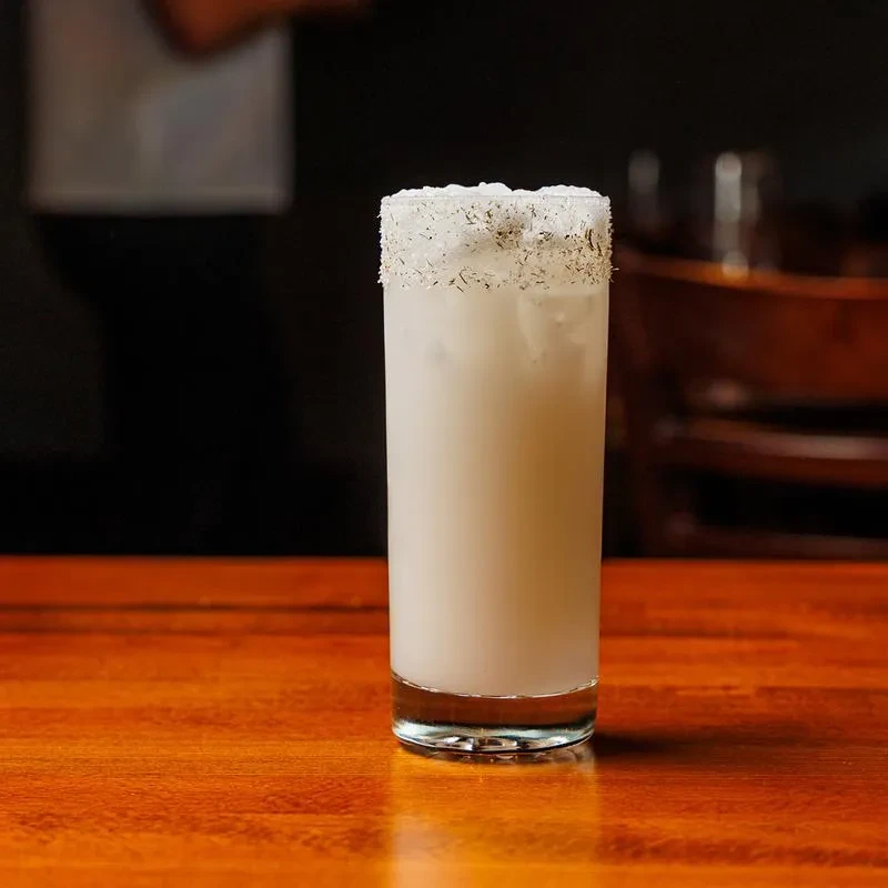 Milky white cocktail with ice and garnished rim on a wooden table.