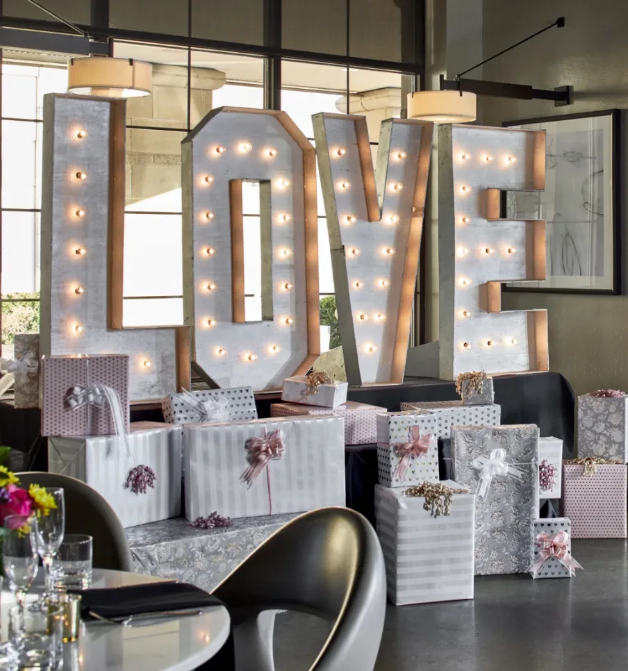 Illuminated "LOVE" marquee sign surrounded by festive wrapped gifts.