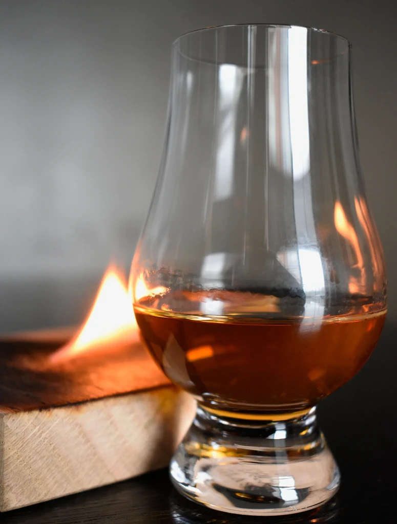 Stemmed glass of amber liquid next to smoking wood.