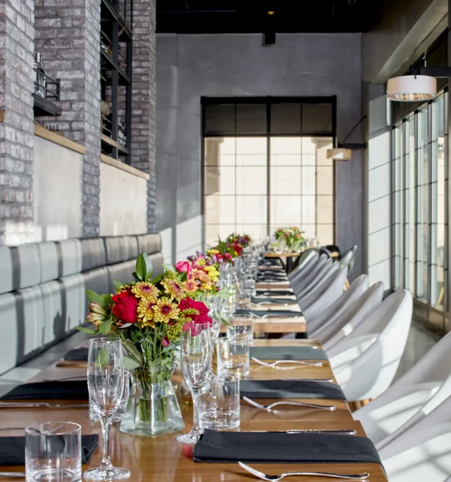 Long wooden table set with flowers in a modern restaurant interior.