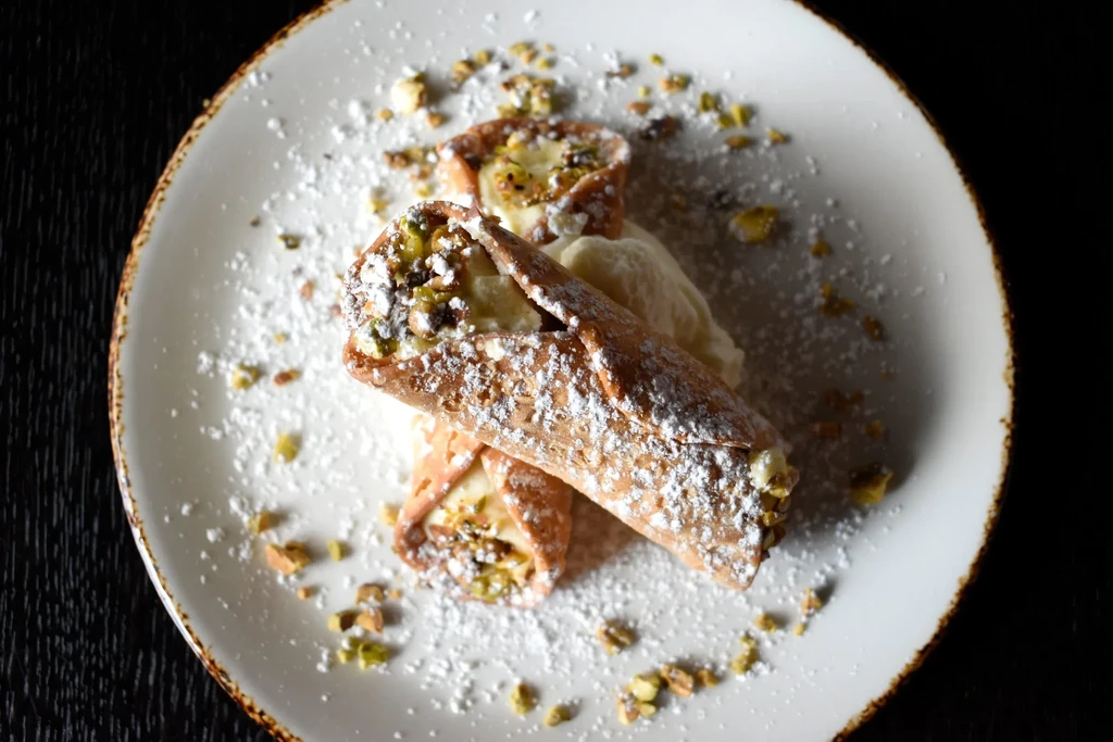 Two cannoli with pistachios, powdered sugar, and cream on a plate.