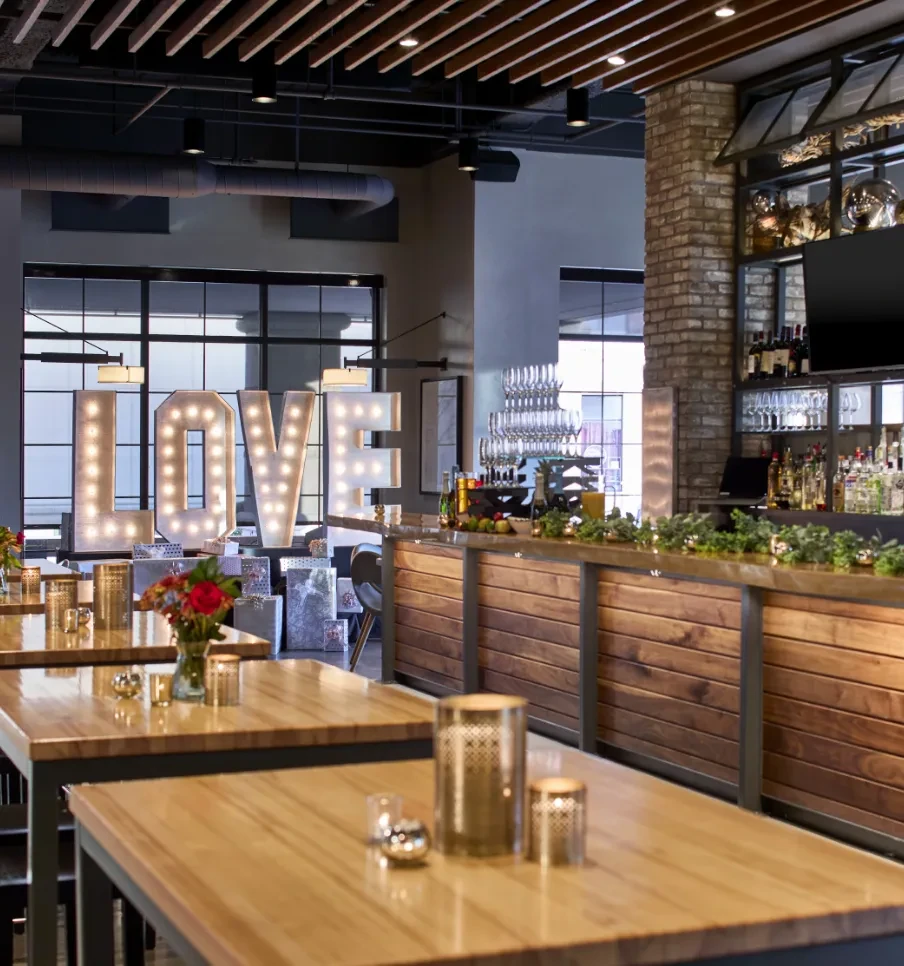 Modern, warm restaurant interior with tables, bar, and 'LOVE' marquee.