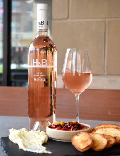 Still life of rosé wine bottle, glass, and appetizers on dark table.