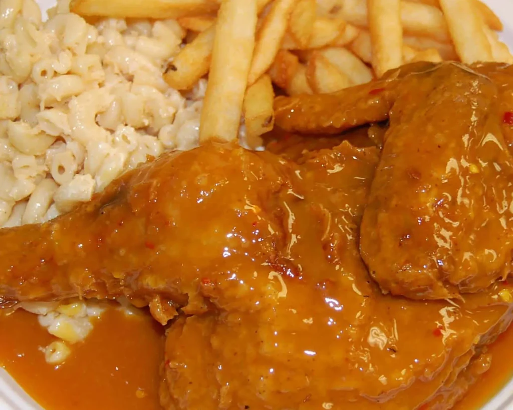 Chicken in orange-brown sauce, french fries, and macaroni and cheese.