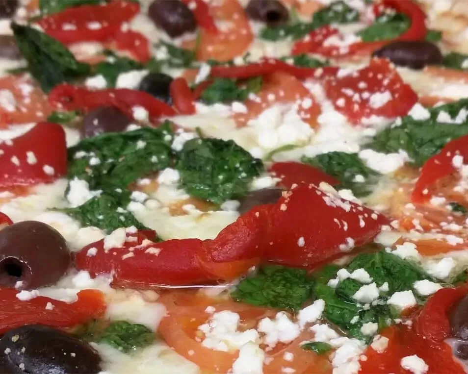 Close-up of pizza with roasted peppers, olives, feta, and greens.