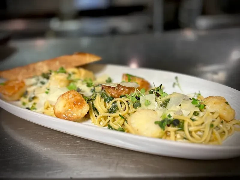 Professionally plated linguine with seared scallops, vegetables, Parmesan, and bread.