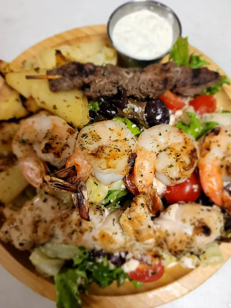 Grilled shrimp, chicken, and souvlaki platter with salad and roasted potatoes.