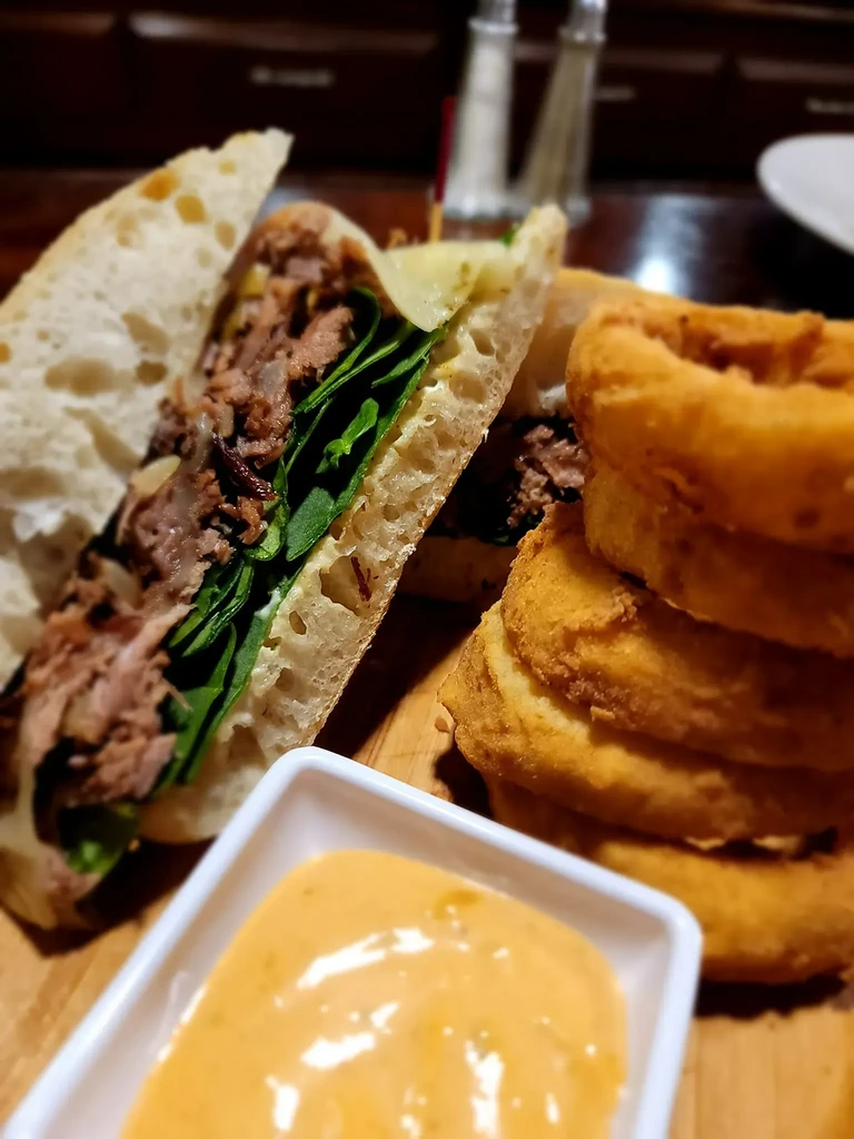 Shredded meat and greens sandwich, onion rings, and dipping sauce.