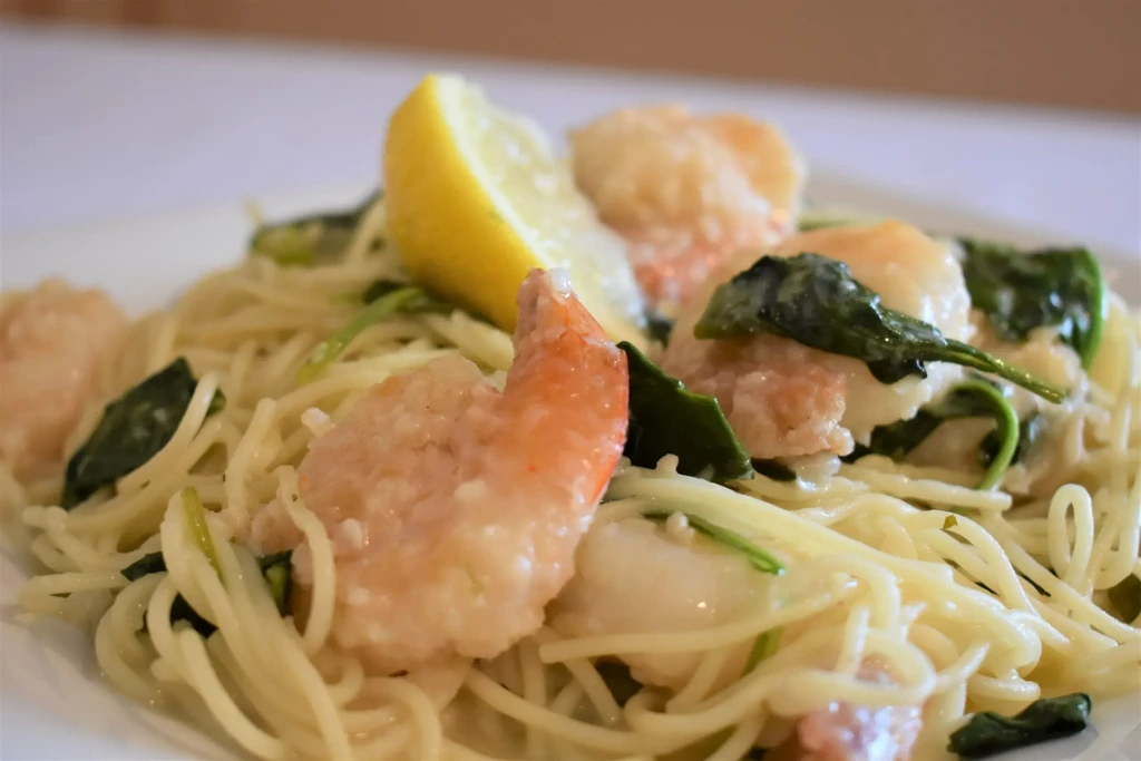 Close-up of spaghetti with shrimp, spinach, lemon wedge, and creamy sauce.