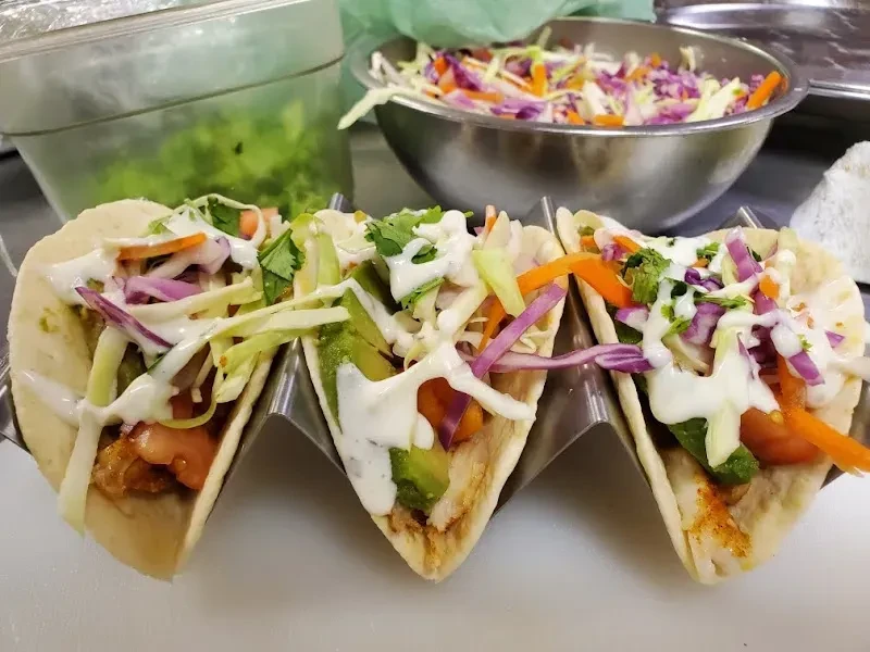 Three soft tacos with colorful toppings in a metal holder.