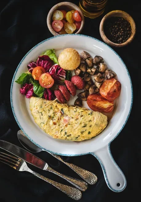 Skillet-plate breakfast with omelette, salad, sausage, mushrooms, and roasted tomatoes.
