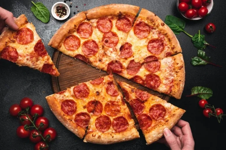 Two hands lifting slices of pepperoni pizza with tomatoes and basil.